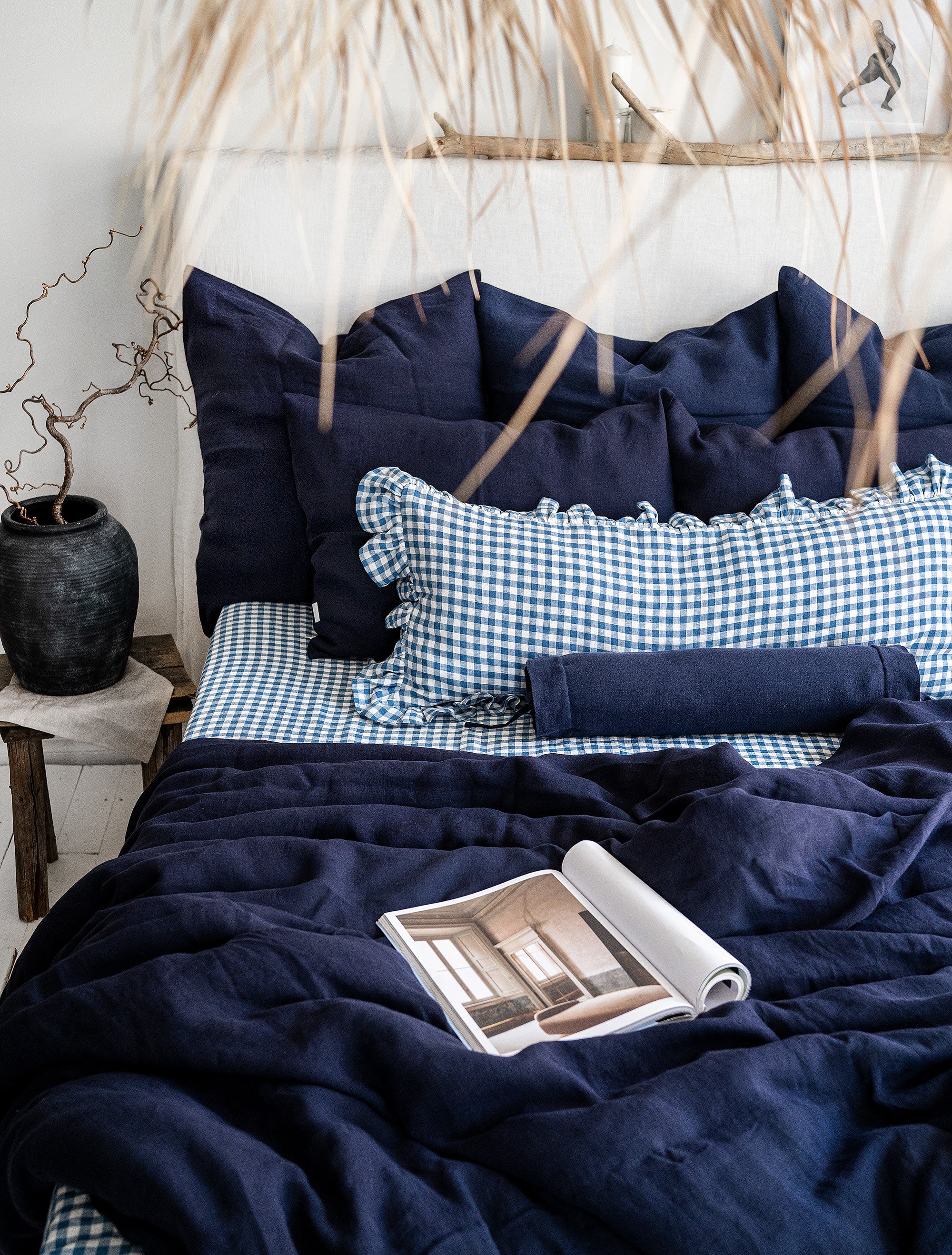 Navy blue bedding with checkered pillows on a bed, featuring a magazine.1621243260e1af0c20-2